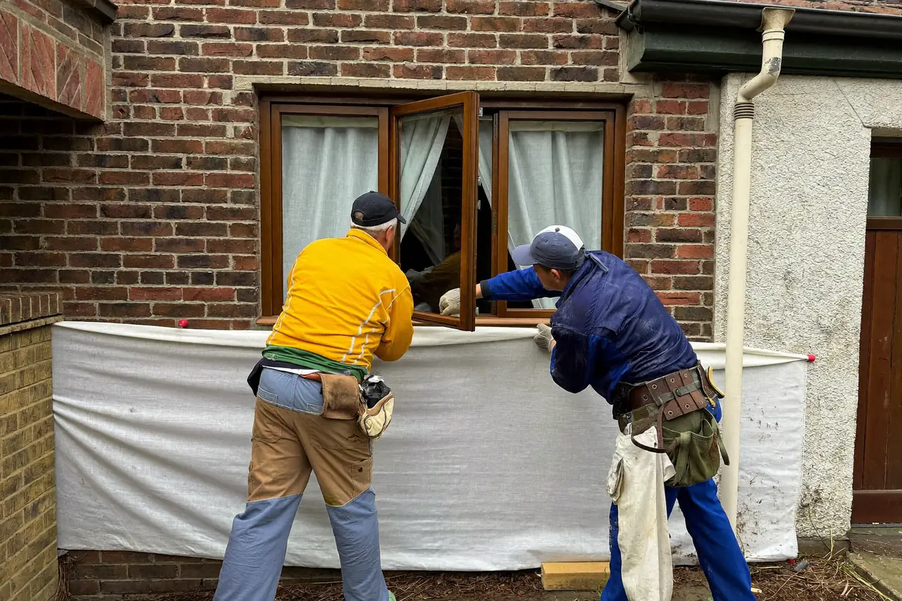 Two fitters carefully removing an old window from a brick wall